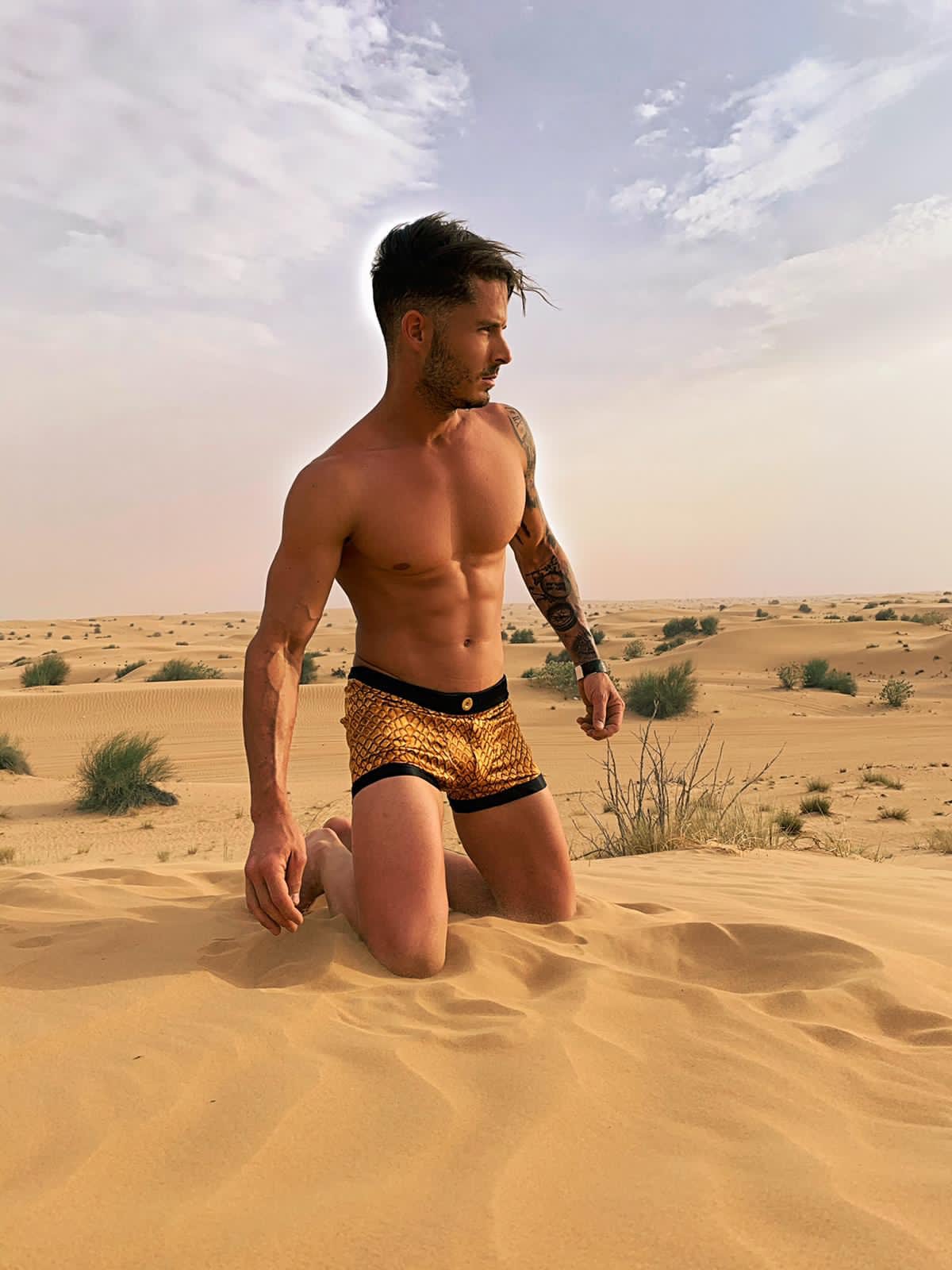 Modèle masculin agenouillé dans le désert, portant le boxer "Gold Croco" de By Radouane, avec un motif crocodile doré sur soie lyonnaise, évoquant luxe et exotisme.