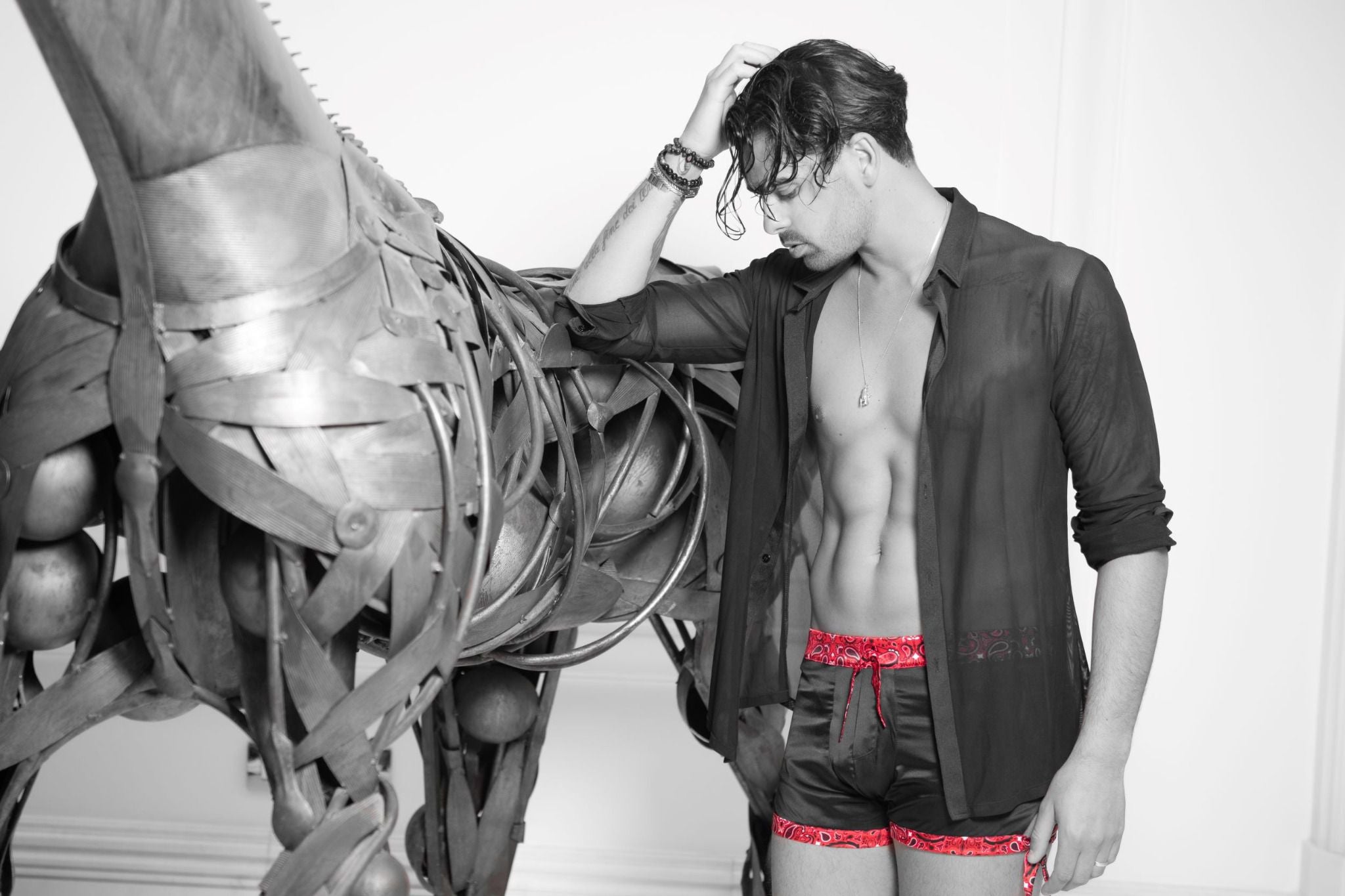 Photo noir et blanc d'un modèle à côté d'une sculpture de cheval, portant un boxer "California Love" By Radouane, mettant en avant la soie noire de qualité et l'accent du bandana rouge iconique.