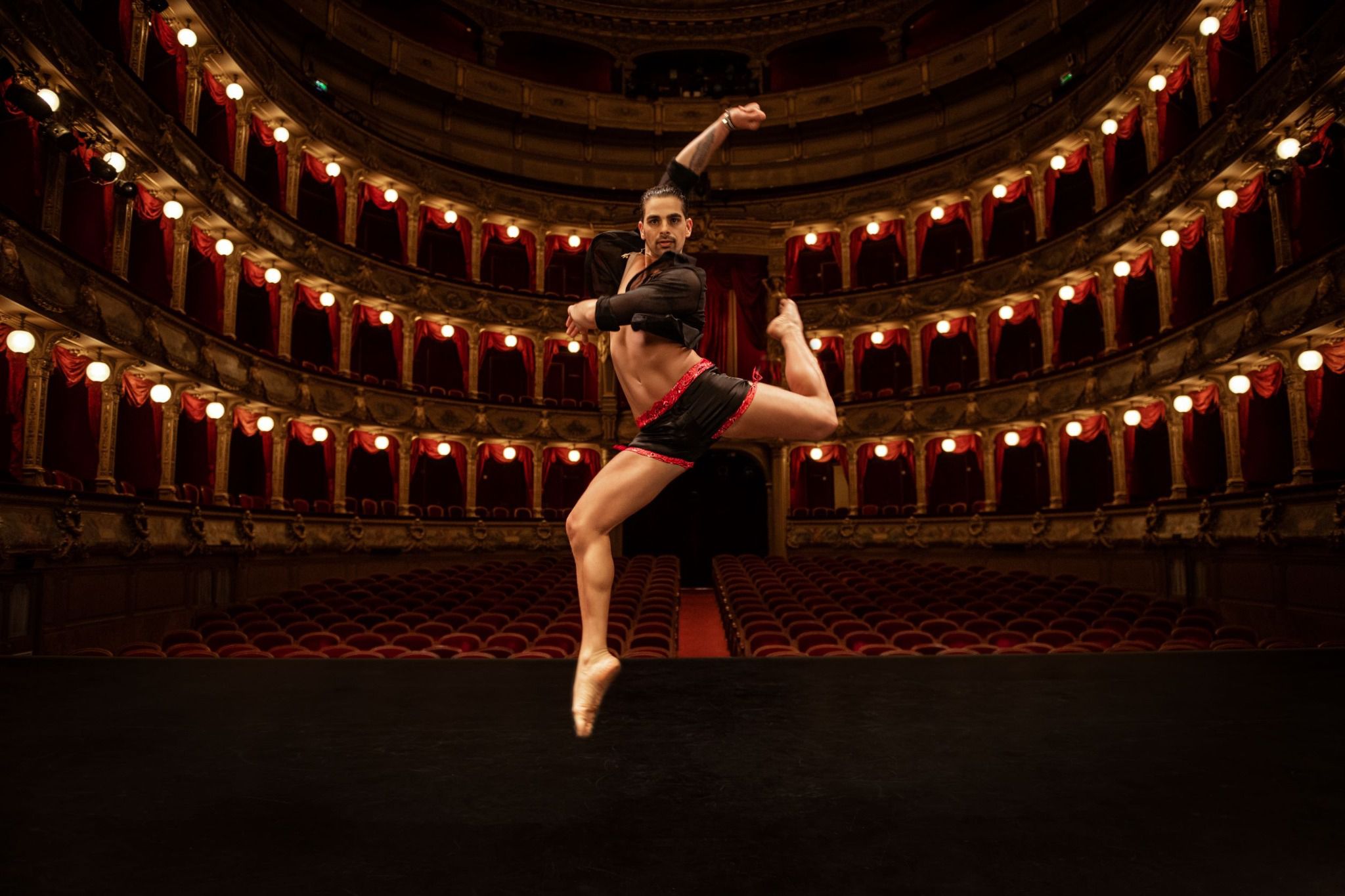 Modèle en position de danse sur une scène de théâtre, vêtu du boxer "California Love" By Radouane, alliant l'athlétisme à l'élégance de la soie noire et au motif bandana rouge.